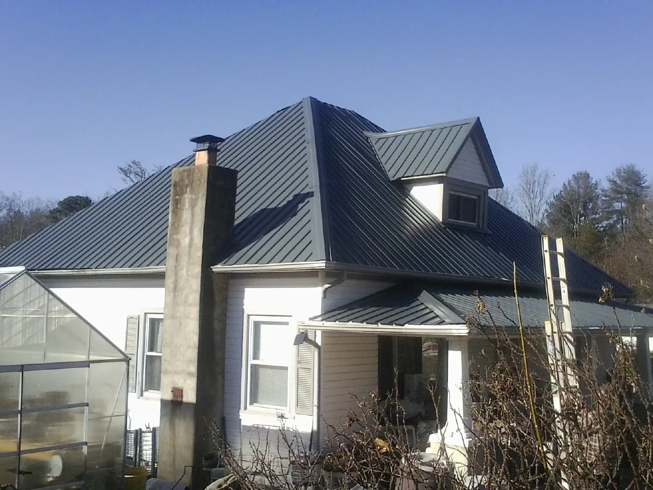 Dark blue standing seam metal roof on a white farmhouse with dormer — Slate & Tile Roof Repair by Roofing Brothers in Ossining
