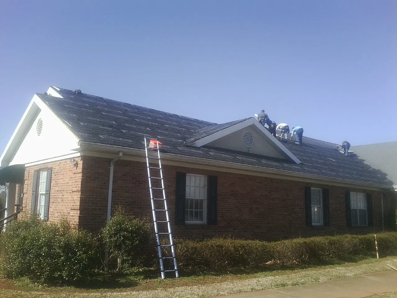 Crew tearing shingles off a brick ranch roof with a ladder set — Metal Roof Repair work by our crew in Ossining