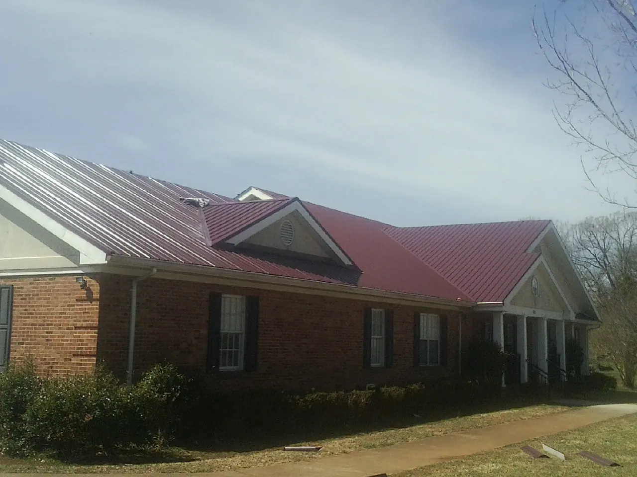 Red metal roof with gabled entries on a long brick building, from a Hail Damage Roof Repair job in Ossining