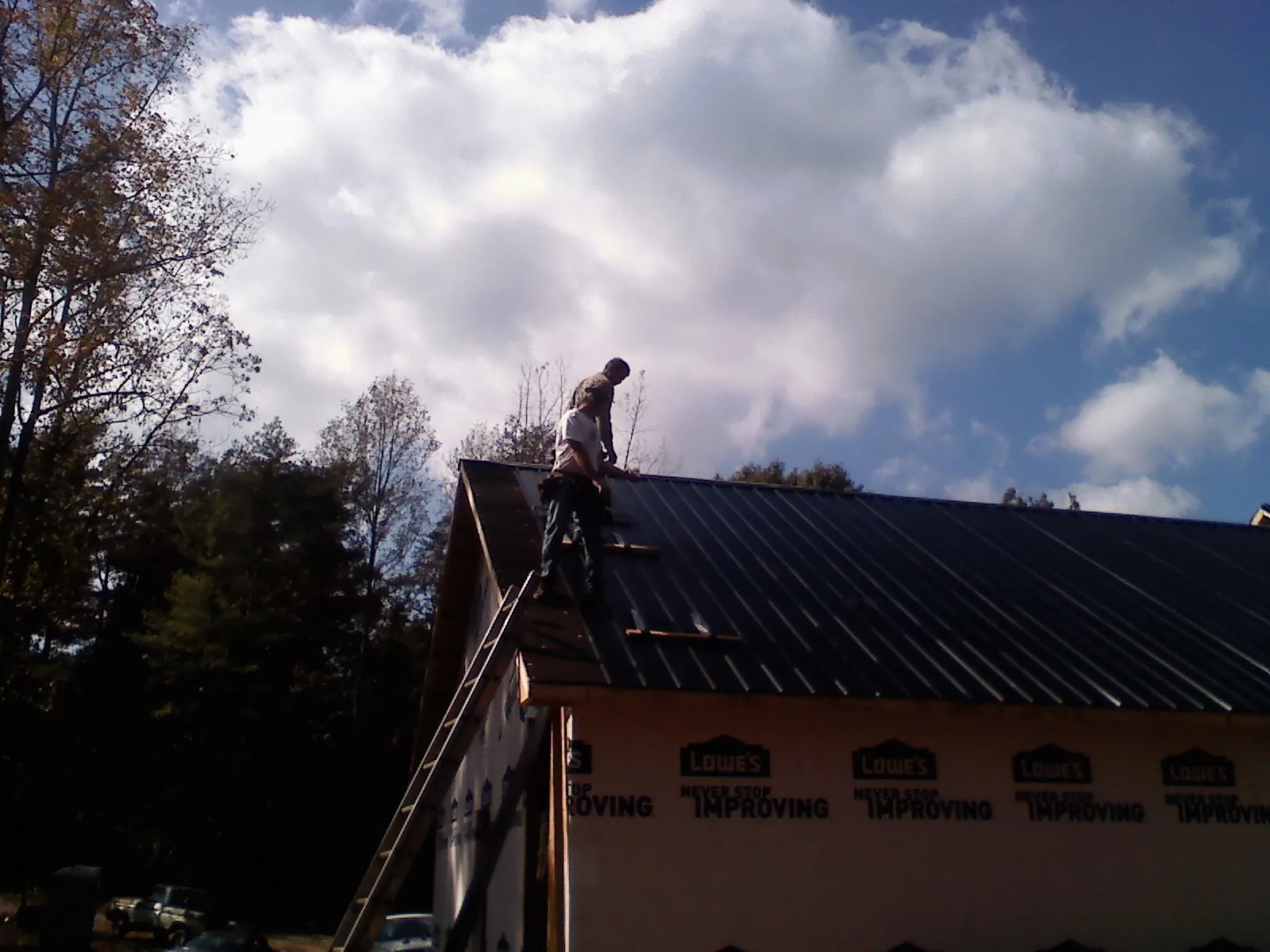Roofer fastening dark metal panels high against a cloudy sky, from a Roof Inspection job in Ossining